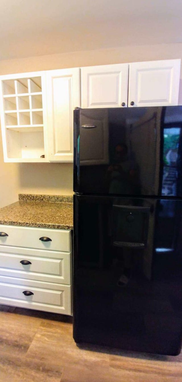 interior space featuring light stone counters, white cabinetry, wood finished floors, and freestanding refrigerator