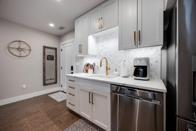 kitchen with a sink, stainless steel appliances, light stone counters, and dark wood-type flooring