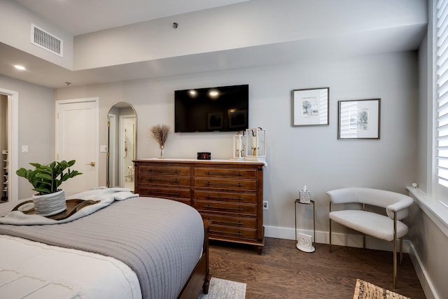 bedroom with dark wood-type flooring, visible vents, arched walkways, and baseboards