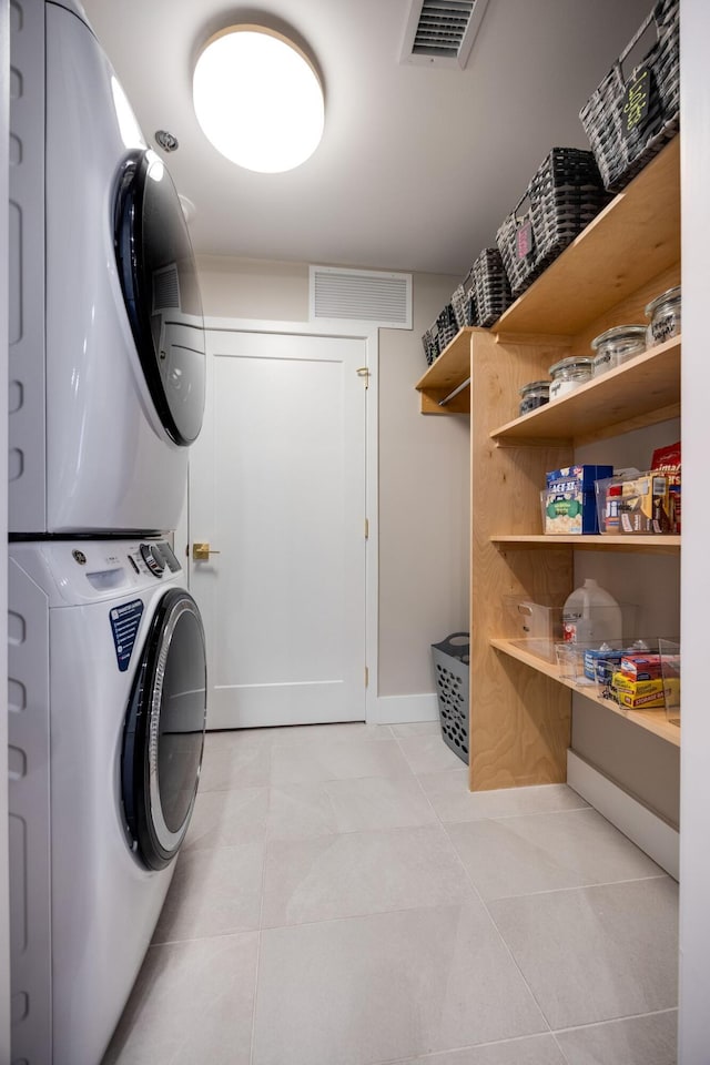 laundry area featuring visible vents, light tile patterned flooring, laundry area, and stacked washing maching and dryer