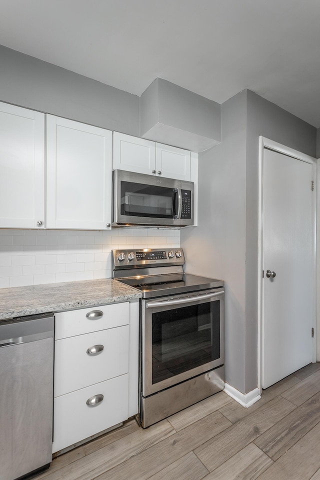 kitchen featuring light stone counters, light wood finished floors, appliances with stainless steel finishes, white cabinetry, and backsplash