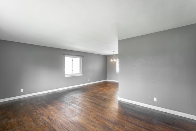 spare room with baseboards, dark wood-style flooring, and a chandelier