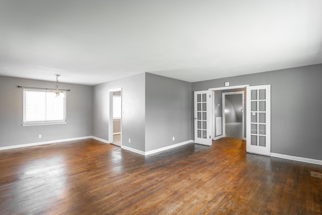 spare room with an inviting chandelier, french doors, dark wood-type flooring, and baseboards