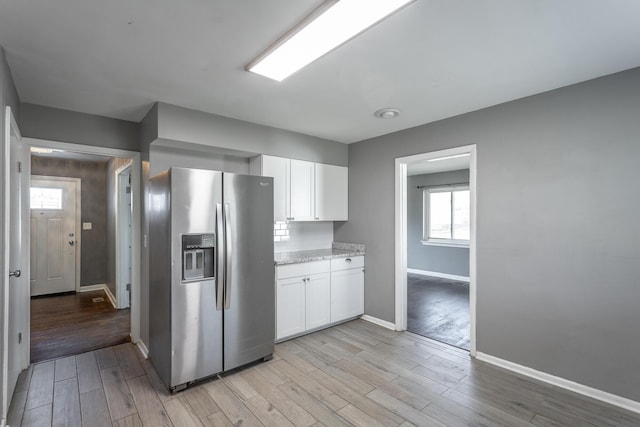 kitchen with baseboards, light stone counters, light wood-style flooring, stainless steel fridge, and white cabinetry