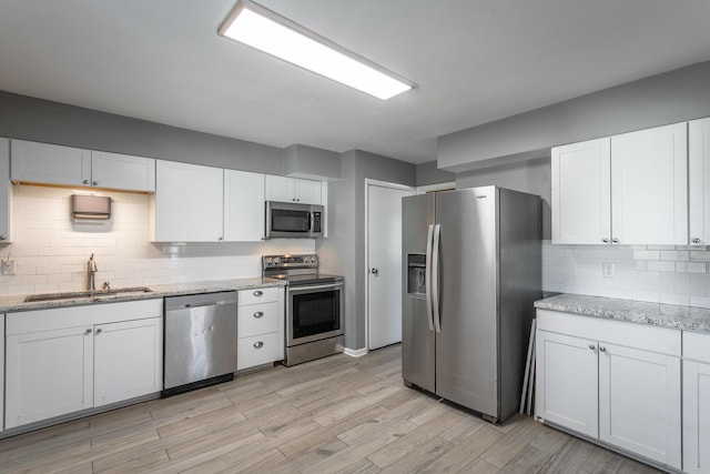 kitchen featuring white cabinets, stainless steel appliances, light wood-type flooring, and a sink