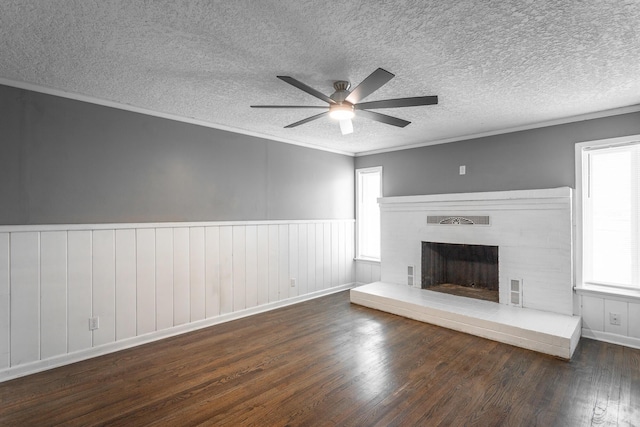 unfurnished living room with wood finished floors, wainscoting, ornamental molding, a textured ceiling, and a brick fireplace