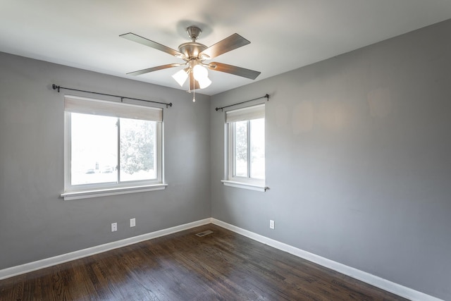 spare room featuring dark wood finished floors, visible vents, a ceiling fan, and baseboards