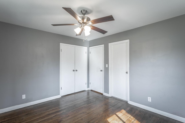 unfurnished bedroom with ceiling fan, two closets, dark wood-type flooring, and baseboards