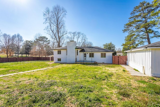 rear view of house with a gate, a lawn, fence, and a chimney