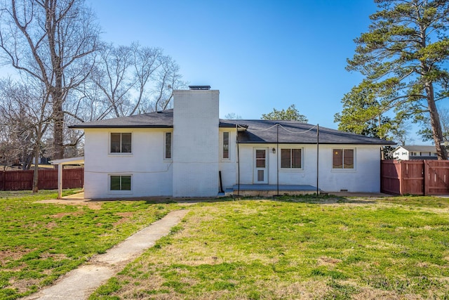 back of house with a yard, brick siding, a chimney, and fence