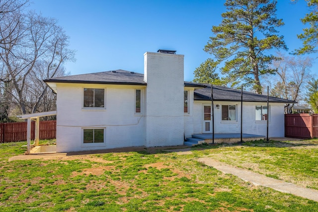 rear view of property featuring brick siding, fence, a chimney, a yard, and a patio