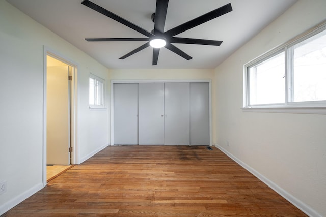 unfurnished bedroom with baseboards, light wood-type flooring, multiple windows, and a closet