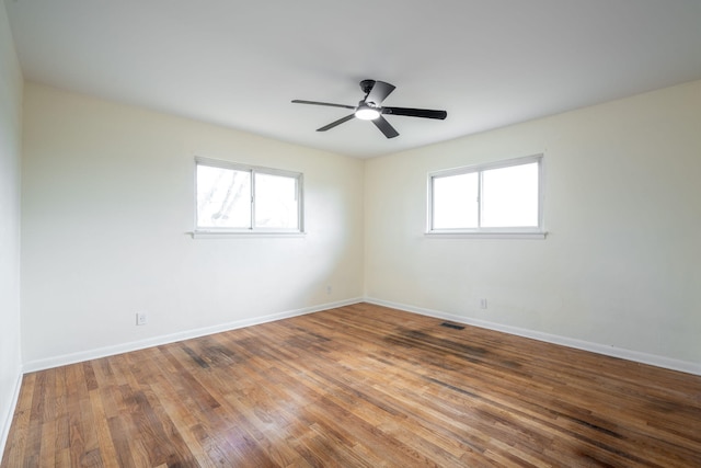 empty room featuring wood finished floors, visible vents, a wealth of natural light, and baseboards