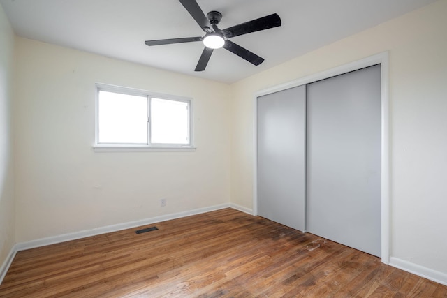 unfurnished bedroom featuring wood finished floors, visible vents, a closet, and baseboards