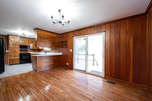 kitchen with brown cabinetry, visible vents, a peninsula, black appliances, and a notable chandelier