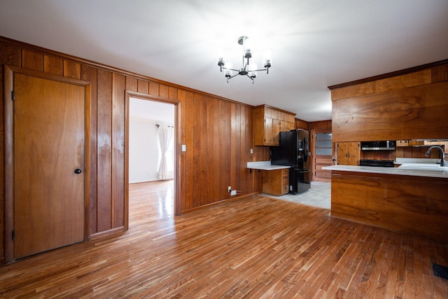 kitchen featuring brown cabinetry, light wood-style flooring, light countertops, a notable chandelier, and black fridge