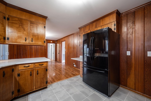 kitchen featuring brown cabinetry, wooden walls, light countertops, and freestanding refrigerator