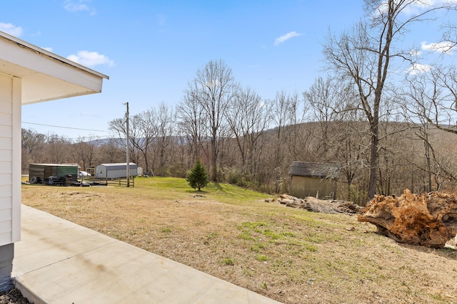 view of yard featuring an outbuilding, a wooded view, and a shed