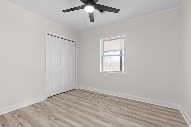 unfurnished bedroom with a closet, light wood-style flooring, crown molding, and baseboards