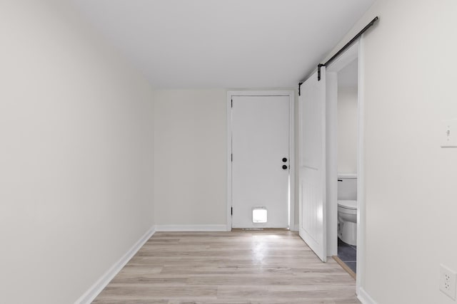 spare room featuring a barn door, light wood-style flooring, and baseboards