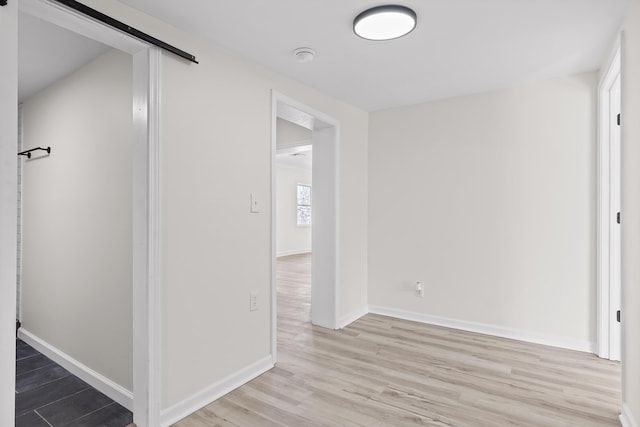 corridor with a barn door, baseboards, and wood finished floors