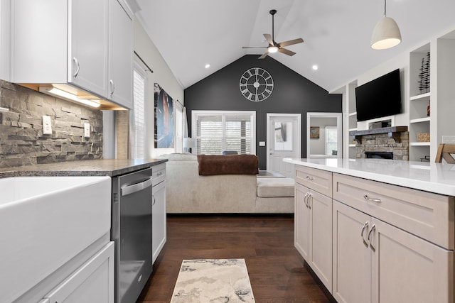 kitchen featuring open floor plan, a stone fireplace, dishwasher, ceiling fan, and dark wood-style flooring