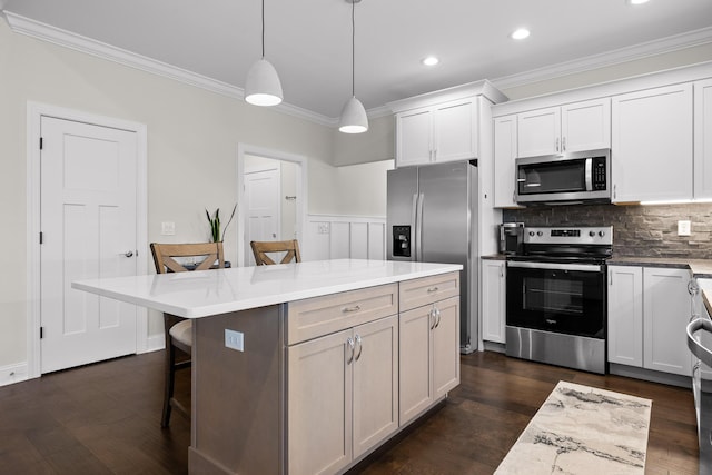 kitchen featuring dark wood-type flooring, a breakfast bar, ornamental molding, white cabinetry, and appliances with stainless steel finishes