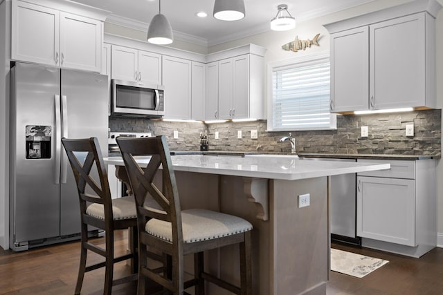 kitchen with ornamental molding, backsplash, a center island, appliances with stainless steel finishes, and a breakfast bar area