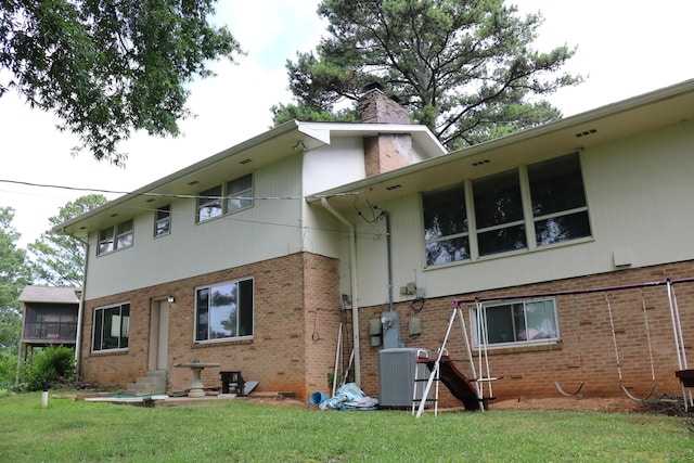 rear view of house featuring a yard, central AC unit, brick siding, and a chimney