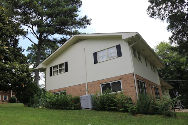 view of side of home featuring brick siding, central air condition unit, and a lawn