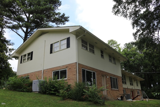 view of property exterior featuring a yard, cooling unit, and brick siding