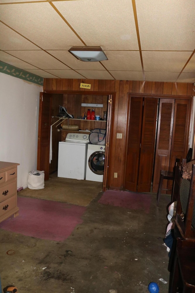 basement with a drop ceiling, wood walls, and washer and clothes dryer