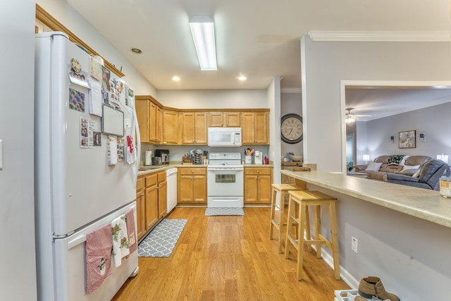 kitchen featuring a kitchen bar, light wood-style flooring, white appliances, crown molding, and light countertops