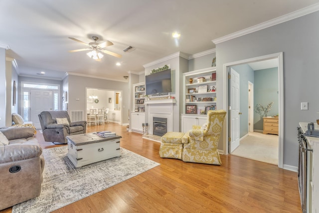 living area with a glass covered fireplace, light wood-style flooring, a ceiling fan, and visible vents