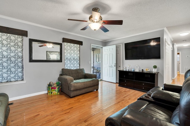 living room featuring light wood finished floors, ceiling fan, baseboards, ornamental molding, and a textured ceiling