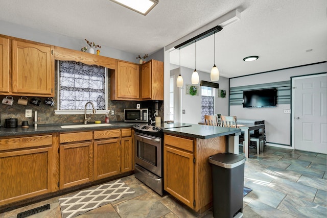 kitchen featuring visible vents, a peninsula, a sink, appliances with stainless steel finishes, and dark countertops