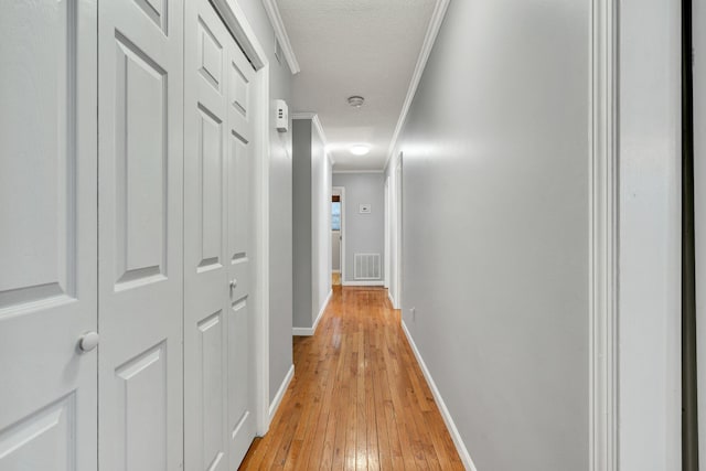 hall with baseboards, visible vents, light wood-style flooring, ornamental molding, and a textured ceiling