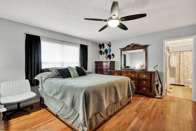 bedroom featuring ensuite bath, a textured ceiling, light wood-type flooring, and a ceiling fan