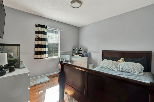 bedroom with baseboards, wood finished floors, visible vents, and a textured ceiling