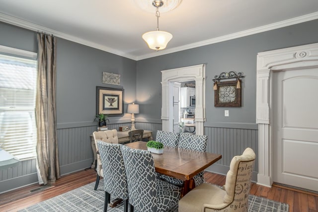 dining space with a wainscoted wall, wood finished floors, and ornamental molding