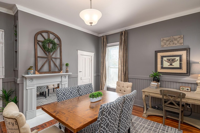 dining area featuring a wainscoted wall, a fireplace, wood finished floors, and crown molding