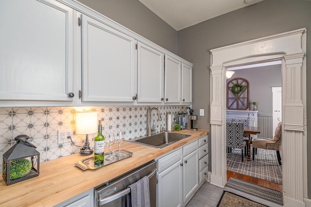 kitchen featuring a sink, backsplash, butcher block countertops, white cabinetry, and stainless steel dishwasher