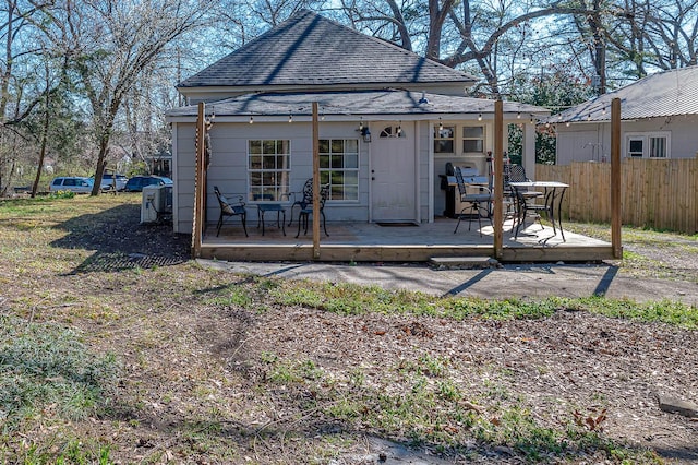 back of house with roof with shingles, a deck, and fence