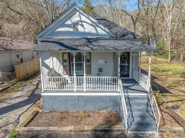 view of front facade with roof with shingles, a porch, and fence