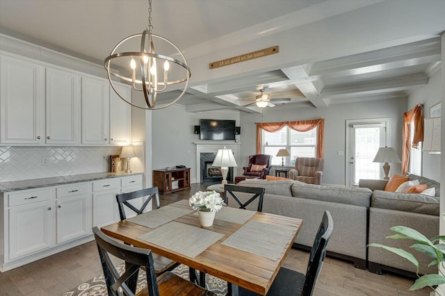 dining space featuring coffered ceiling, light wood-style flooring, a high end fireplace, and ceiling fan with notable chandelier