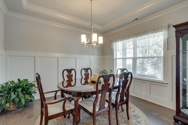 dining area featuring a tray ceiling, a chandelier, dark wood-style flooring, and a decorative wall