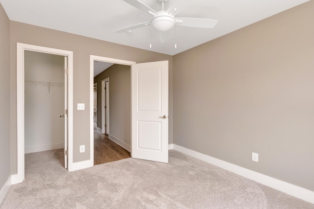 unfurnished bedroom with a spacious closet, ceiling fan, baseboards, carpet flooring, and a closet