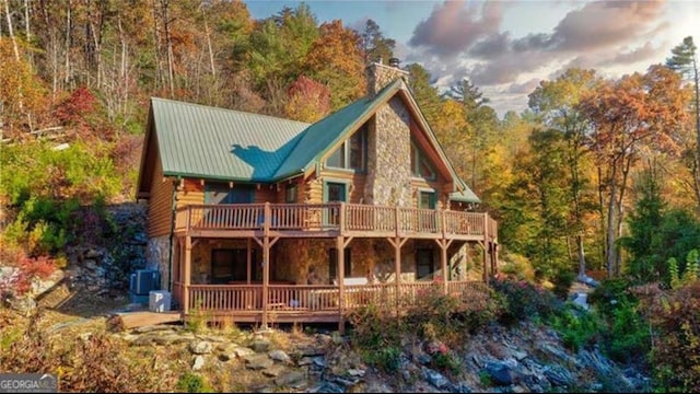 back of house with a wooden deck, log exterior, stone siding, and a chimney