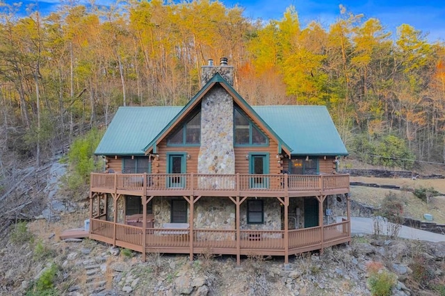 back of property featuring stone siding, log exterior, a chimney, and metal roof