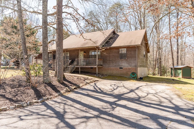 view of front of home with an outbuilding, a shed, covered porch, a shingled roof, and crawl space